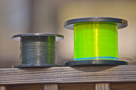 Two spools of fishing line placed on a wooden surface, one with dark green braided line and the other with bright yellow monofilament line, highlighted against a soft blurred background